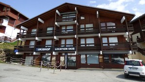 A multi-story building with a ski shop and location signage, wooden balconies, and a car parked in front. - Bright studio cabin in Les Saisies, 4 ppl, south balcony (Les Saisies)