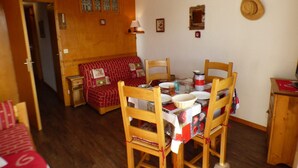 A cozy room with a dining table set for four, wooden chairs, a red sofa, and a wooden cabinet. - Bright studio cabin in Les Saisies, 4 ppl, south balcony (Les Saisies)