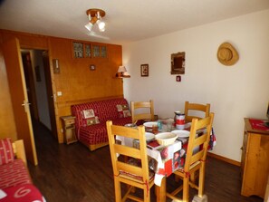Um quarto acolhedor com uma mesa de jantar posta para quatro pessoas, cadeiras de madeira, um sofá vermelho e um armário de madeira.