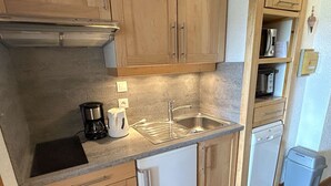A compact kitchen with wooden cabinets, a built-in dishwasher, a coffee maker, and a microwave. - Bright studio cabin in Les Saisies, 4 ppl, south balcony (Les Saisies)