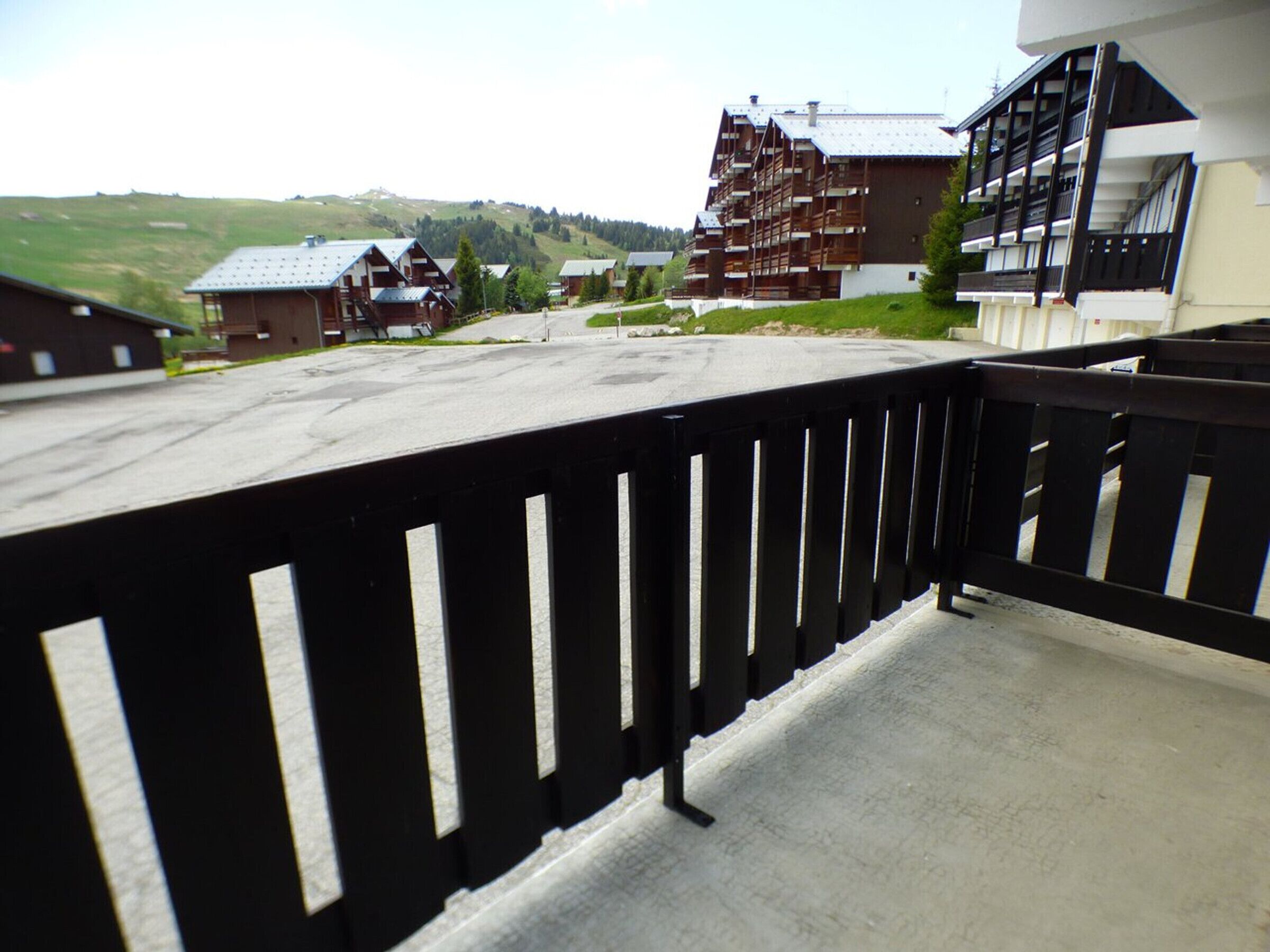 Een balkon met een zwarte reling dat uitkijkt over een parkeerplaats en diverse gebouwen met traditionele architectuur.