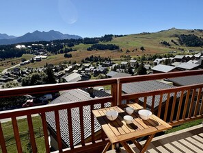 Una terraza de madera con una mesa y sillas, con vistas a un pueblo con casas y montañas al fondo.