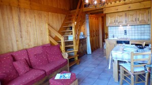A cozy wooden interior with a sofa, a dining table set for two, and a staircase leading to an upper level. - 2-room apartment Les Saisies, top of resort, 6 people, balcony. (Les Saisies)