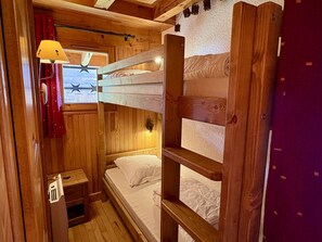 A compact wooden cabin room with bunk beds, a small bedside table, and a window with curtains.