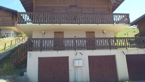 Un chalet en bois à deux étages, doté d’un balcon, d’un escalier et de deux portes de garage.