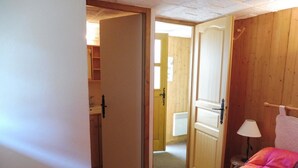 Une chambre à coucher avec un lit, une porte en bois et une salle de bain visible à travers une porte ouverte.