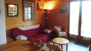 L’intérieur d’un chalet confortable, avec un décor en bois, un canapé, un fauteuil, une table et une fenêtre agrémentée de rideaux.