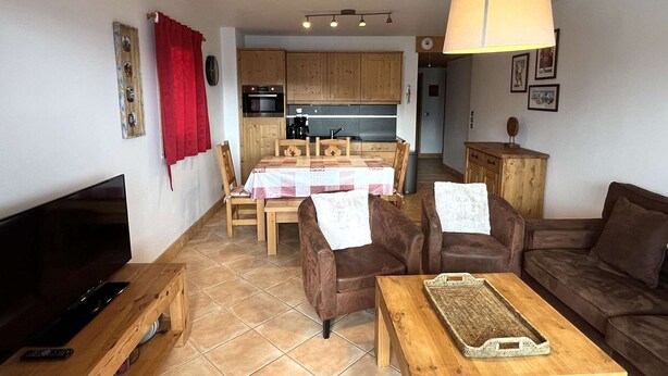 Un salon équipé d’un téléviseur, de canapés en cuir, d’une table basse en bois et d’un coin repas avec une table dressée pour quatre personnes.