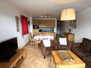 A living room with a TV, leather sofas, a wooden coffee table, and a dining area with a table set for four.