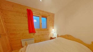 Une chambre à coucher avec une tête de lit en bois, un lit simple, une table de chevet avec une lampe et une fenêtre ornée d’un rideau rouge.