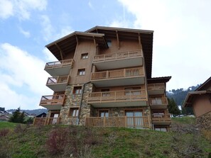 A multi-story building with balconies, stone facade, and a hilly background.
