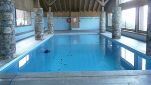 Une piscine intérieure agrémentée de piliers en pierre, de poutres en bois et de grandes fenêtres.