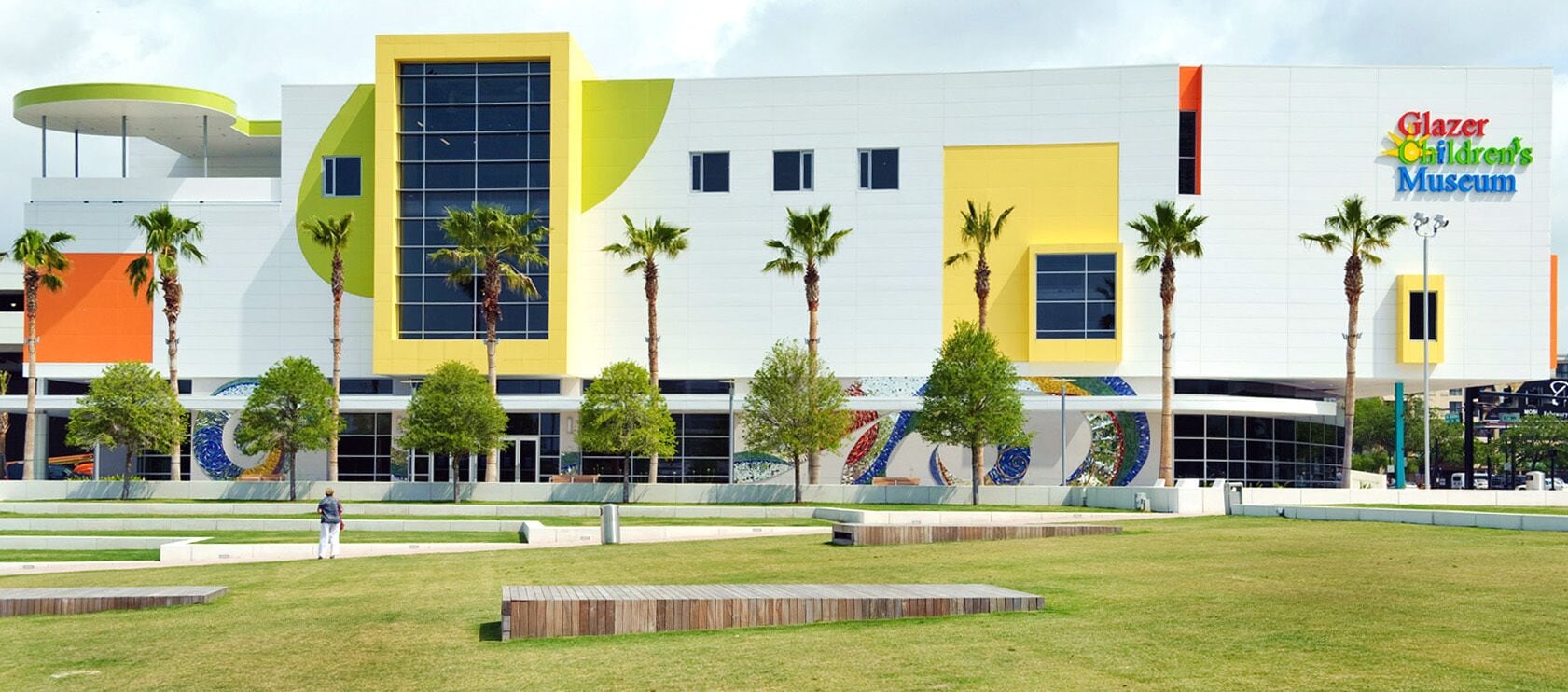 A modern building with a large glass facade, palm trees, and a colorful mural.
