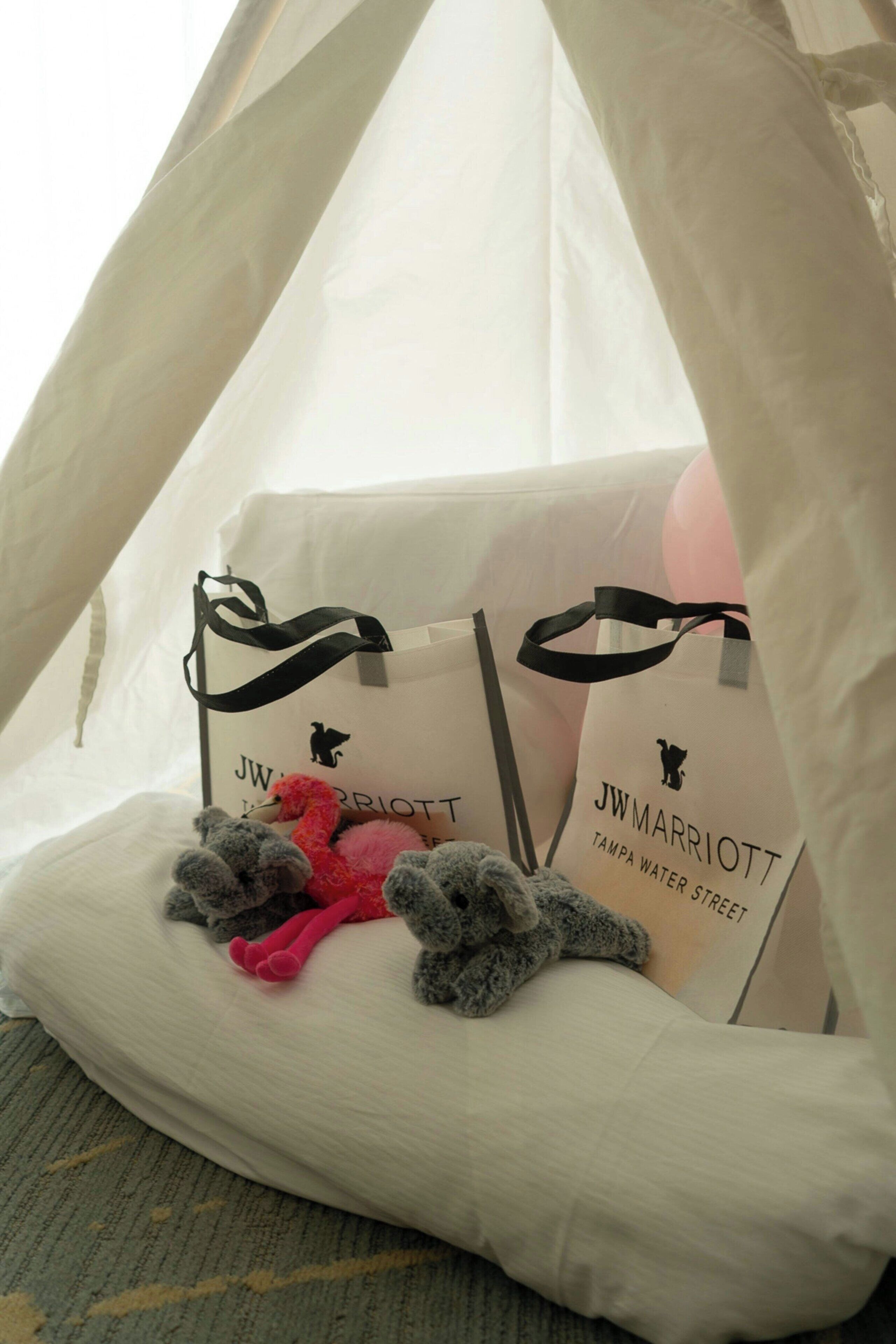 Una estructura tipo tienda de campaña con dos bolsas JW Marriott y peluches en su interior.