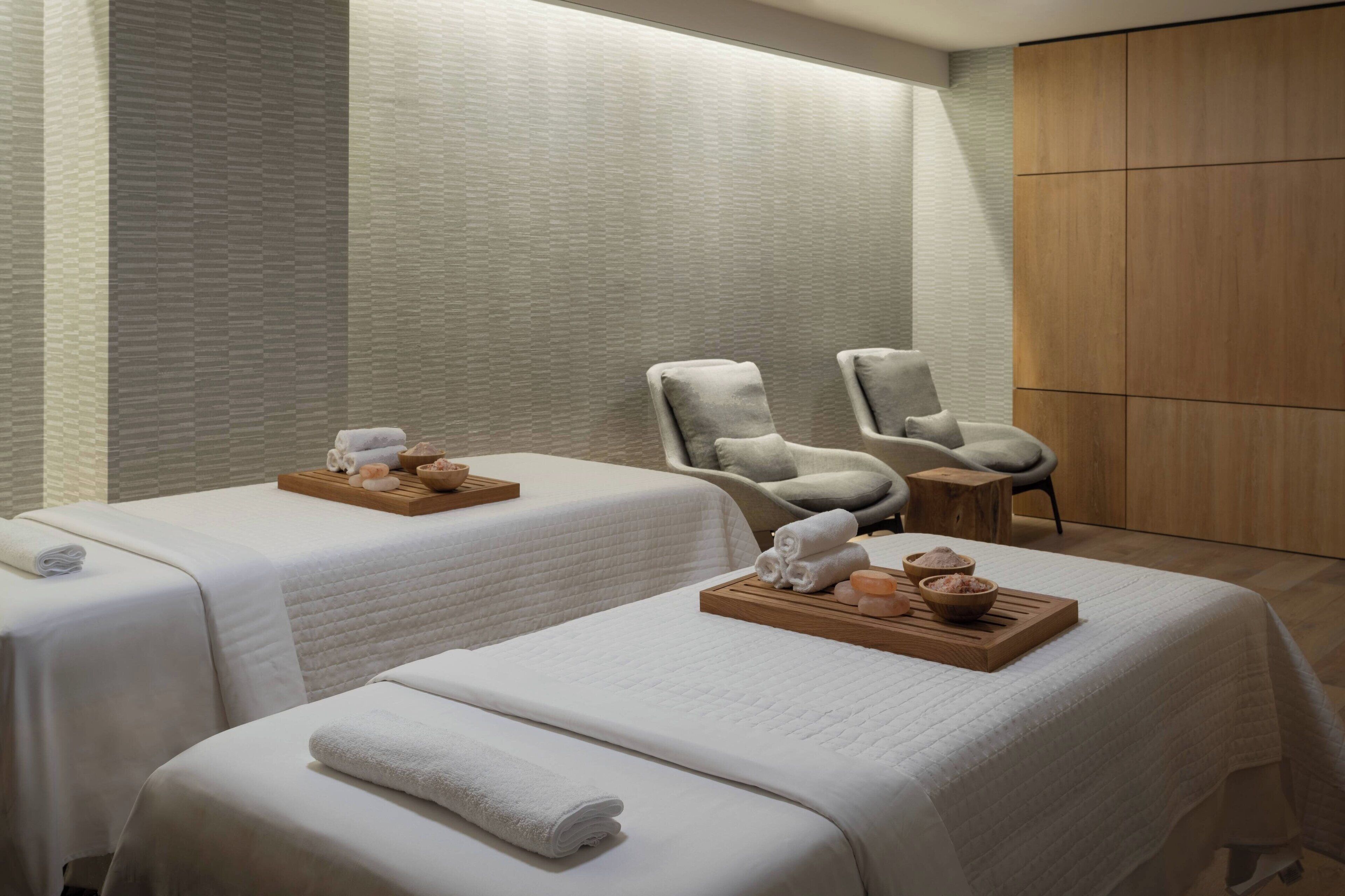 Un cuarto de spa con dos camas, cada una con toallas y una bandeja de productos de baño.