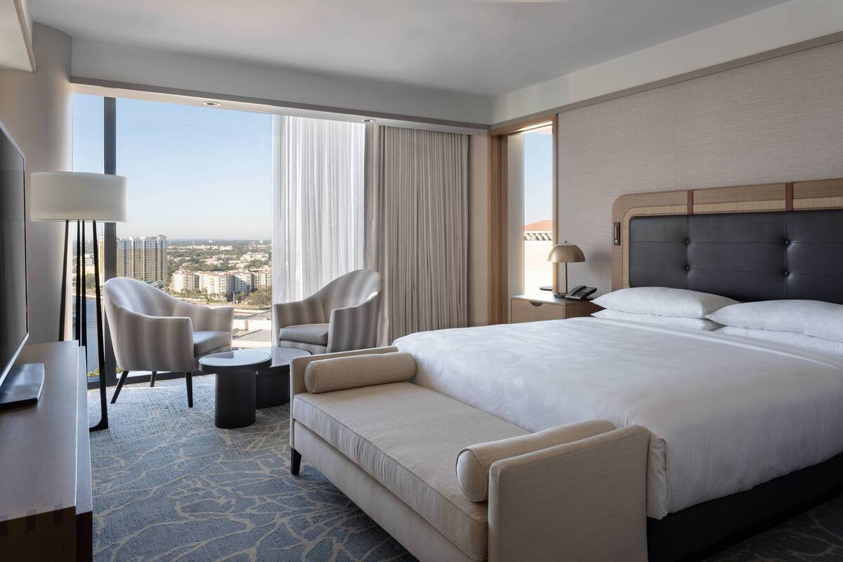 A hotel room with a large bed, two armchairs, a desk, and a view of the city.