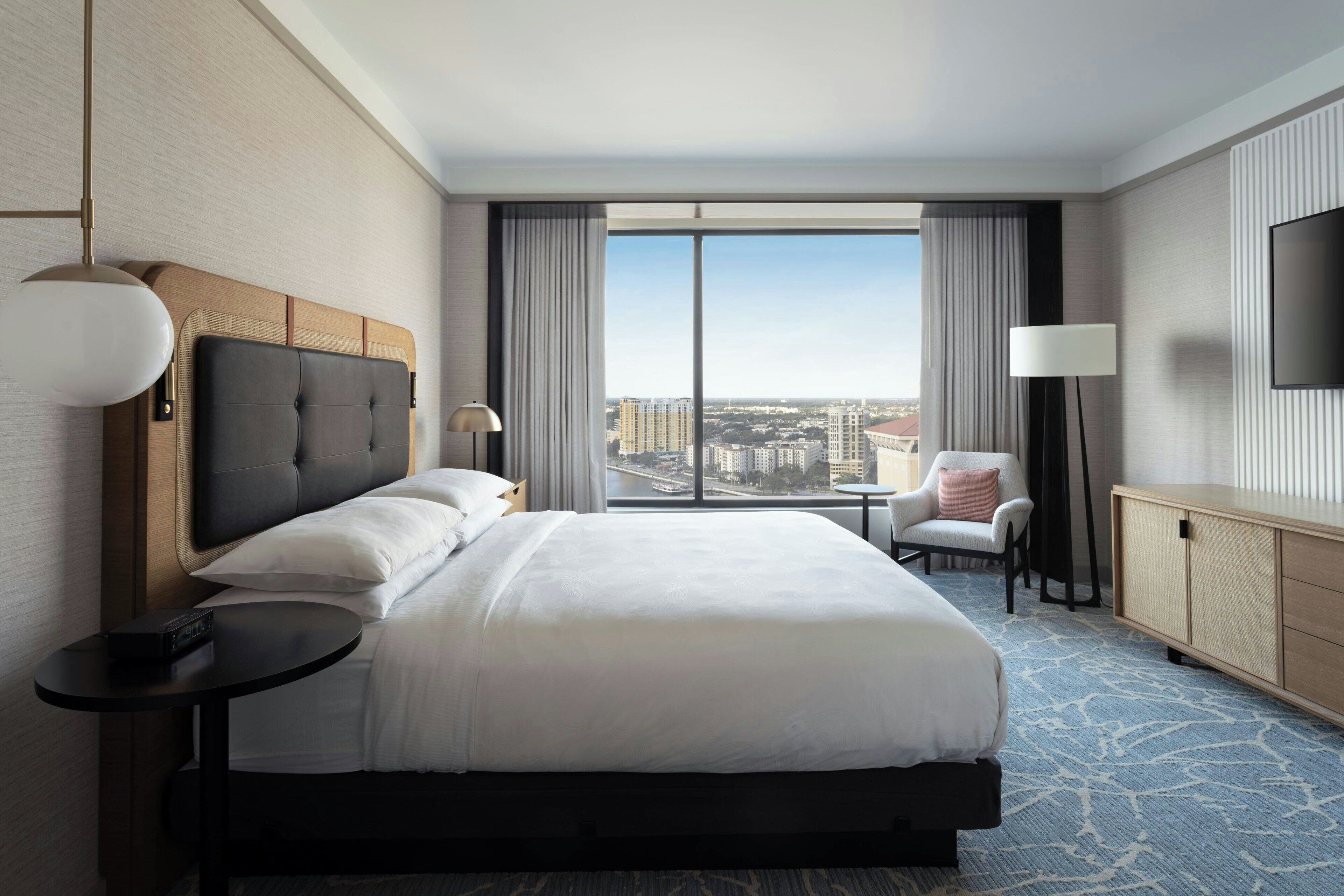 Quarto de hotel com uma cama grande, vista da cidade, uma mesa e uma cadeira.