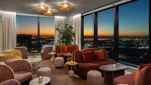 Een moderne lounge met stadszicht, met banken, poefs en ronde tafels.