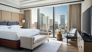 Een moderne hotelkamer met een groot bed, een bank, een televisie en uitzicht over de stad.
