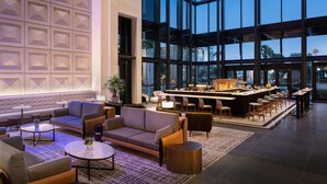 Een moderne hotellobby met een bar, zitgedeeltes en grote ramen.