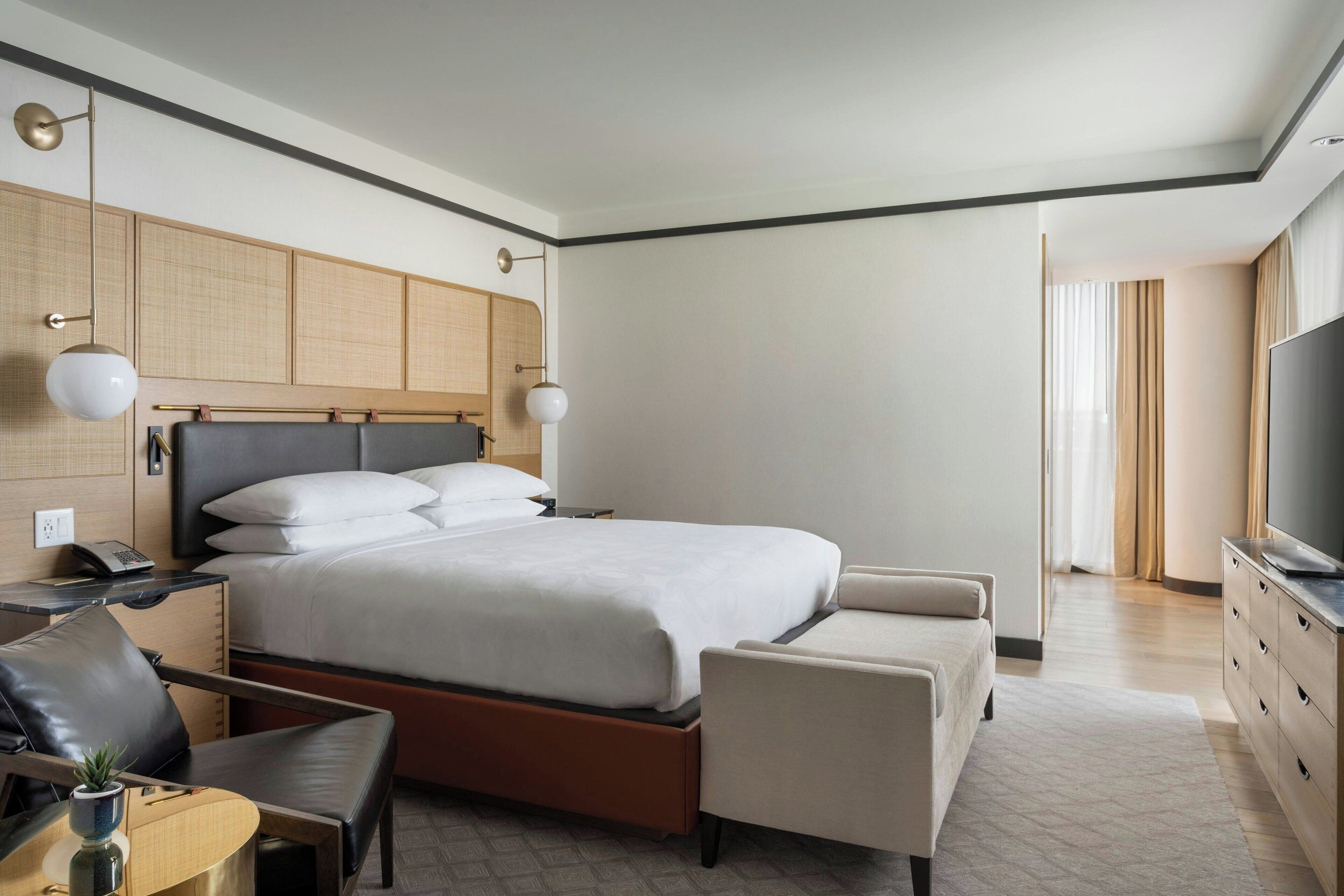 Una habitación de hotel moderna con una cama grande, un escritorio con silla, un televisor y un armario.