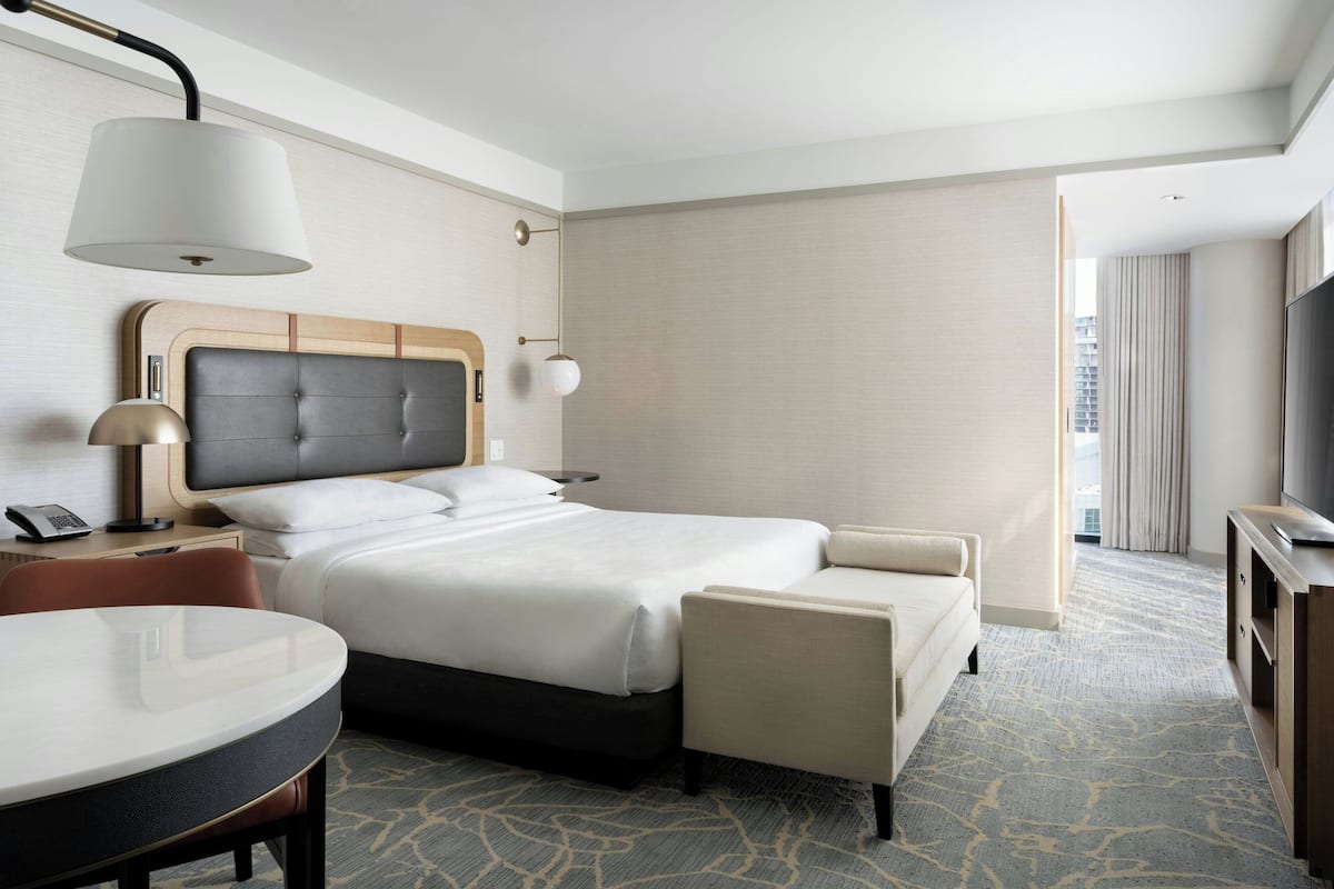 A hotel room with a bed, a desk, a chair, a TV, and a large window.