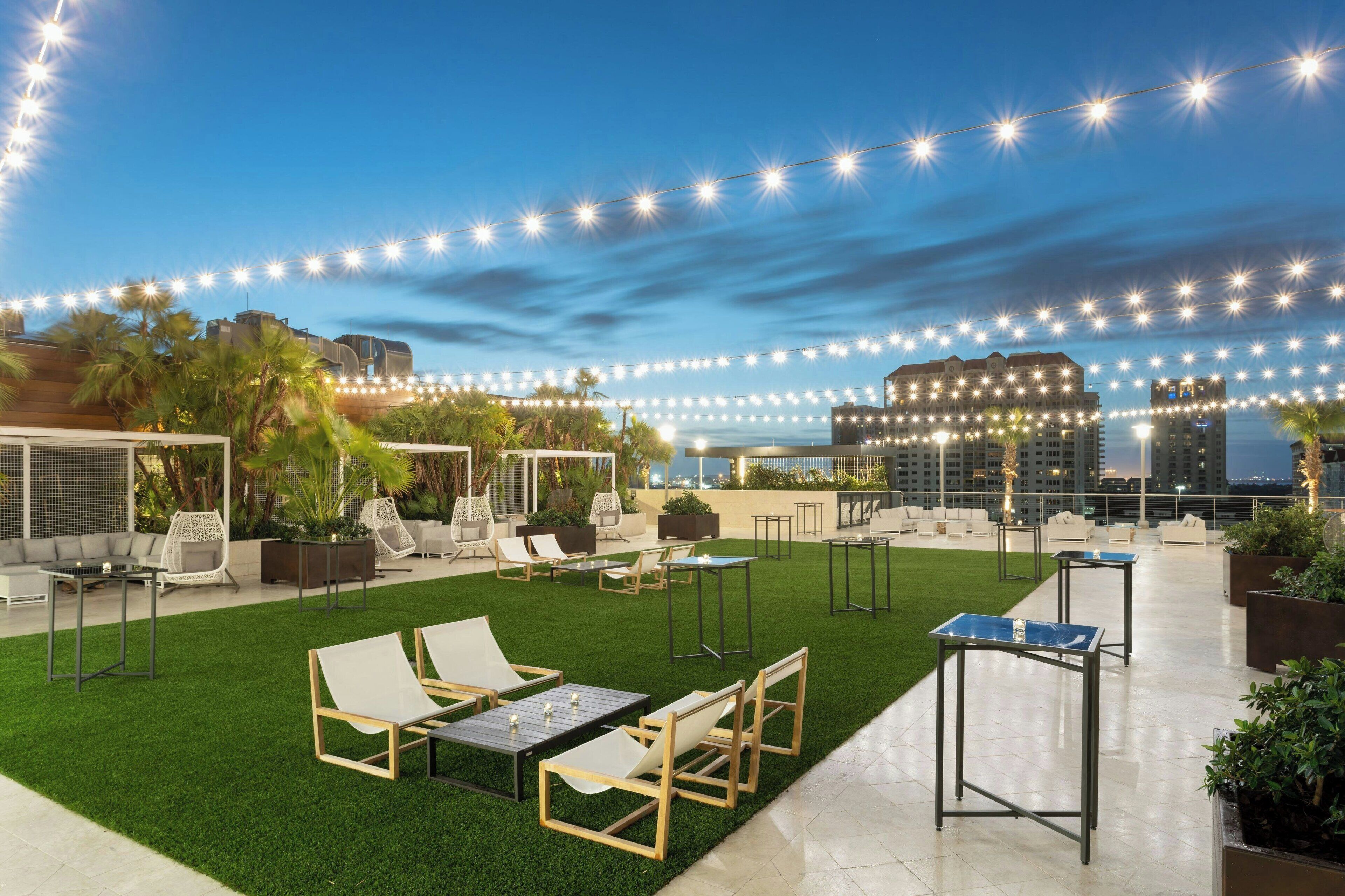 A rooftop terrace with outdoor seating, string lights, and a view of the city skyline.