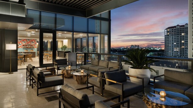 Een moderne rooftop lounge met comfortabele zitplaatsen, grote ramen en een uitzicht op de skyline van de stad in de schemering.