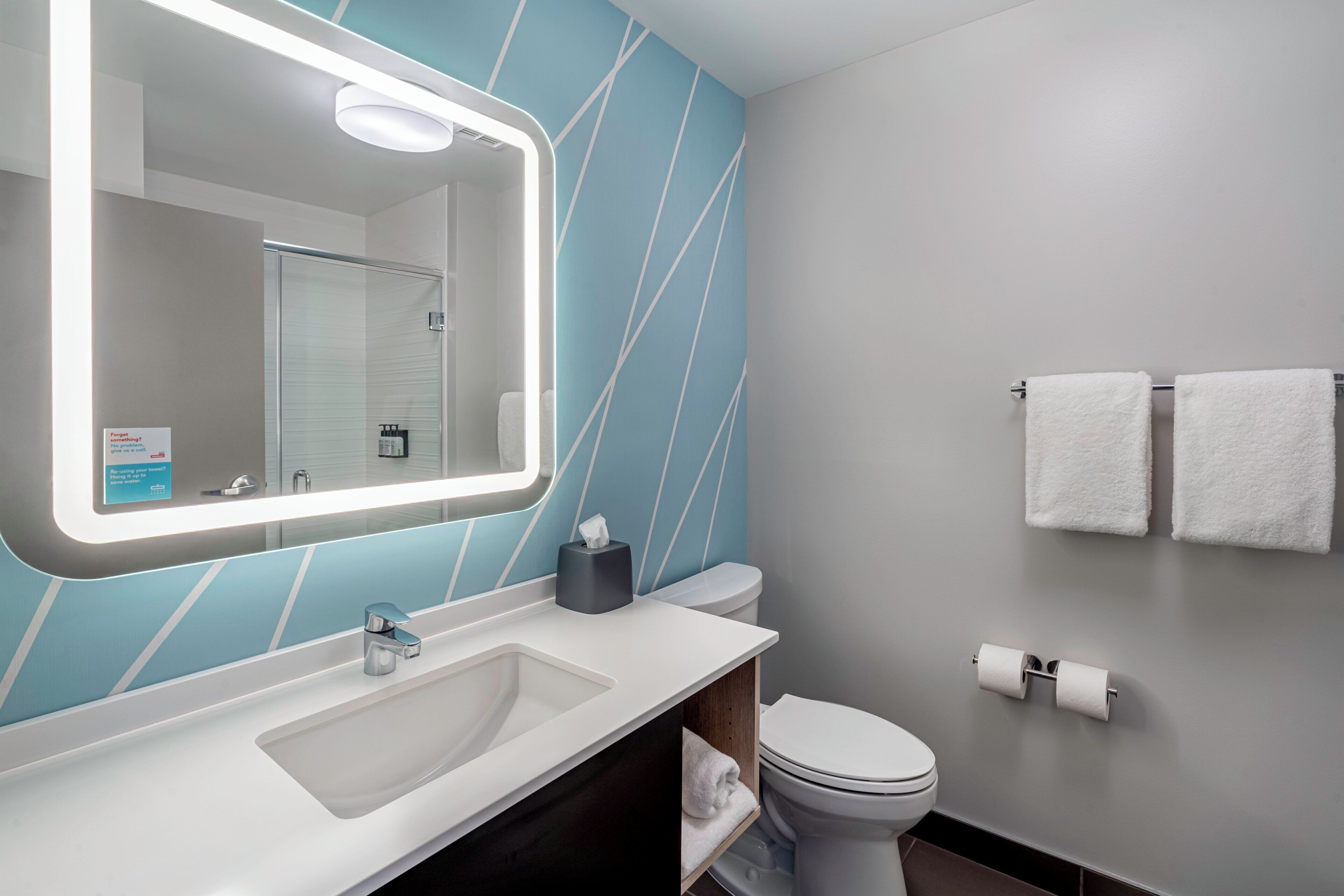 A modern bathroom with a large mirror, a sink, a toilet, and a towel rack.
