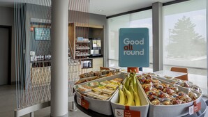 A breakfast buffet with labeled containers of fruits and cereals, a 'Good all round' sign, and a view of the outdoors through large windows. - avid hotel Milwaukee West Waukesha by IHG (Pewaukee)