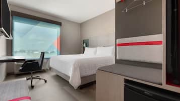 Quarto de hotel com cama, escrivaninha, cadeira, mesa pequena e vista da cidade.