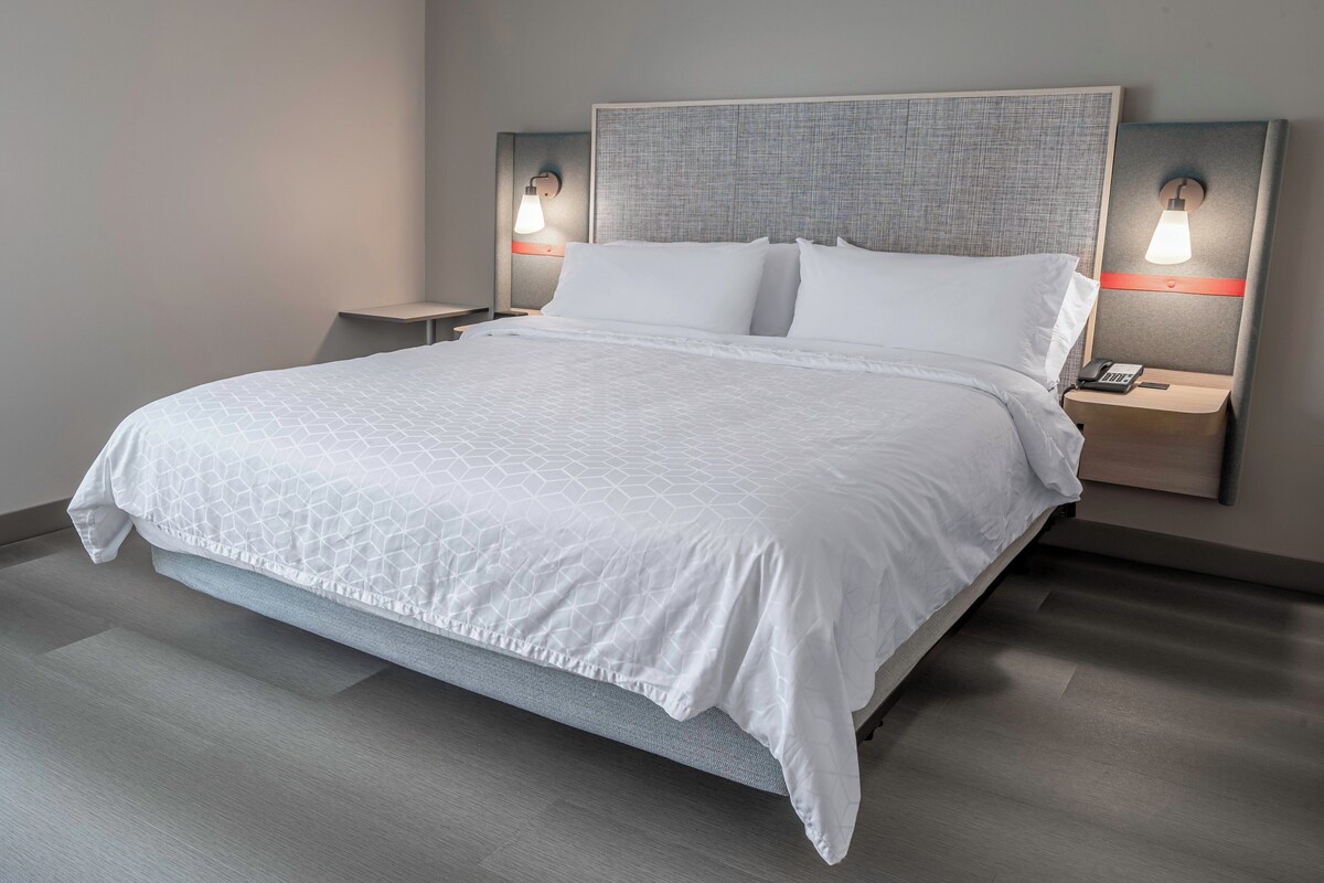 Ein modernes Hotelzimmer mit einem großen Bett, zwei Nachttischen mit Lampen und einer neutralen Farbgestaltung.