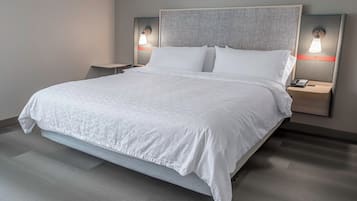 Une chambre d’hôtel moderne avec un grand lit, deux tables de chevet et des lampes fixées au mur.