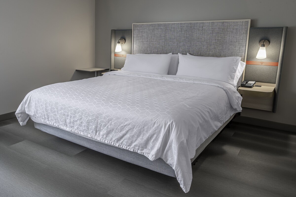 Ein modernes Hotelzimmer mit einem großen Bett, zwei Nachttischen mit Lampen und einer neutralen Farbgestaltung.