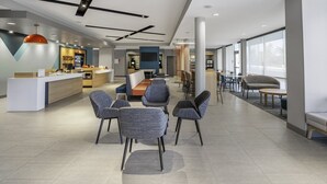 A modern hotel lobby with a reception desk, seating area, and large windows. - avid hotel Milwaukee West Waukesha by IHG (Pewaukee)