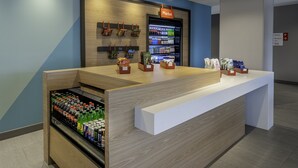 A modern reception desk with a wooden finish, a refrigerated beverage display, and a sign indicating the market area. - avid hotel Milwaukee West Waukesha by IHG (Pewaukee)