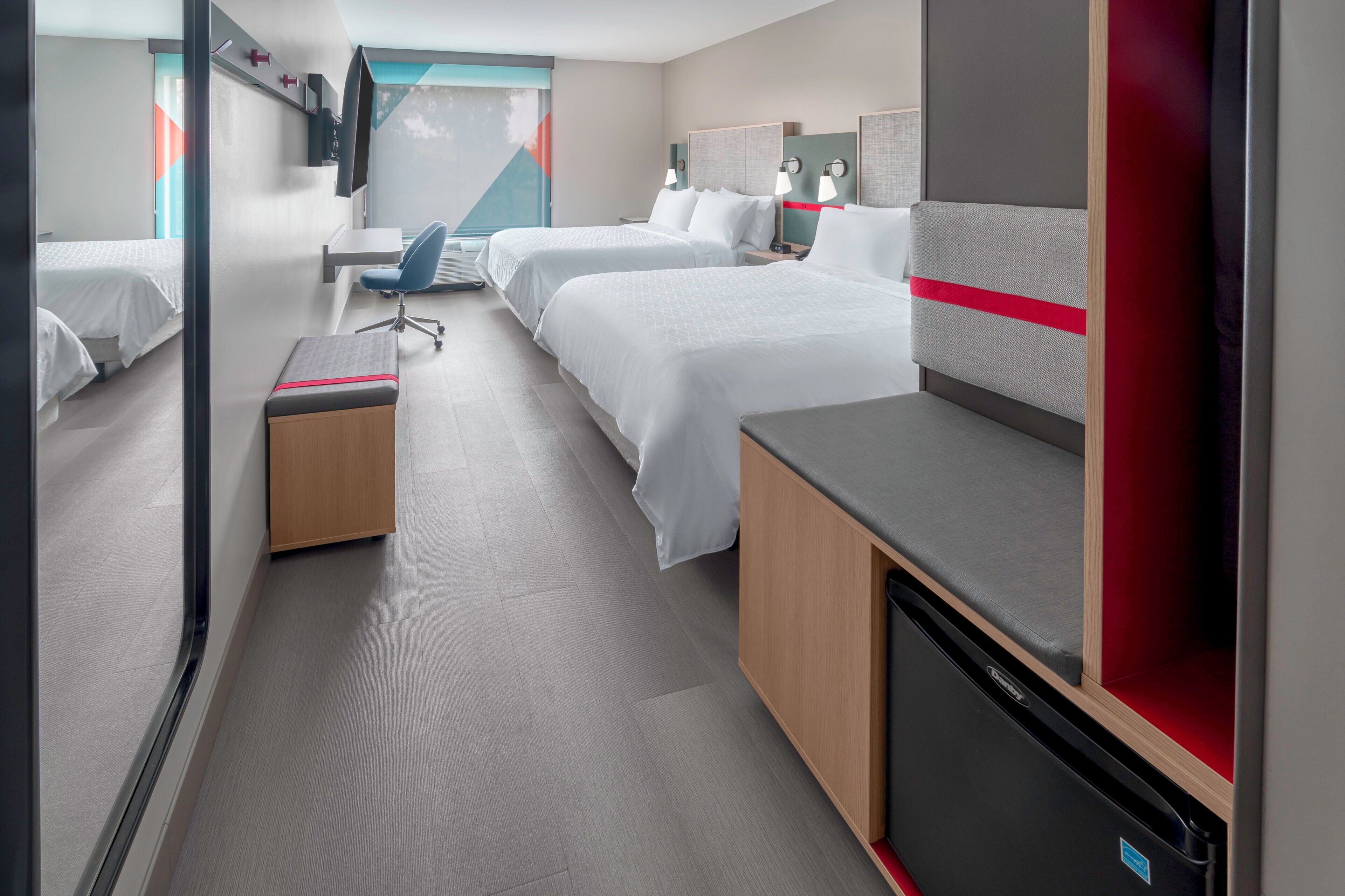 Habitación de hotel con dos camas, un escritorio, una silla y un televisor.