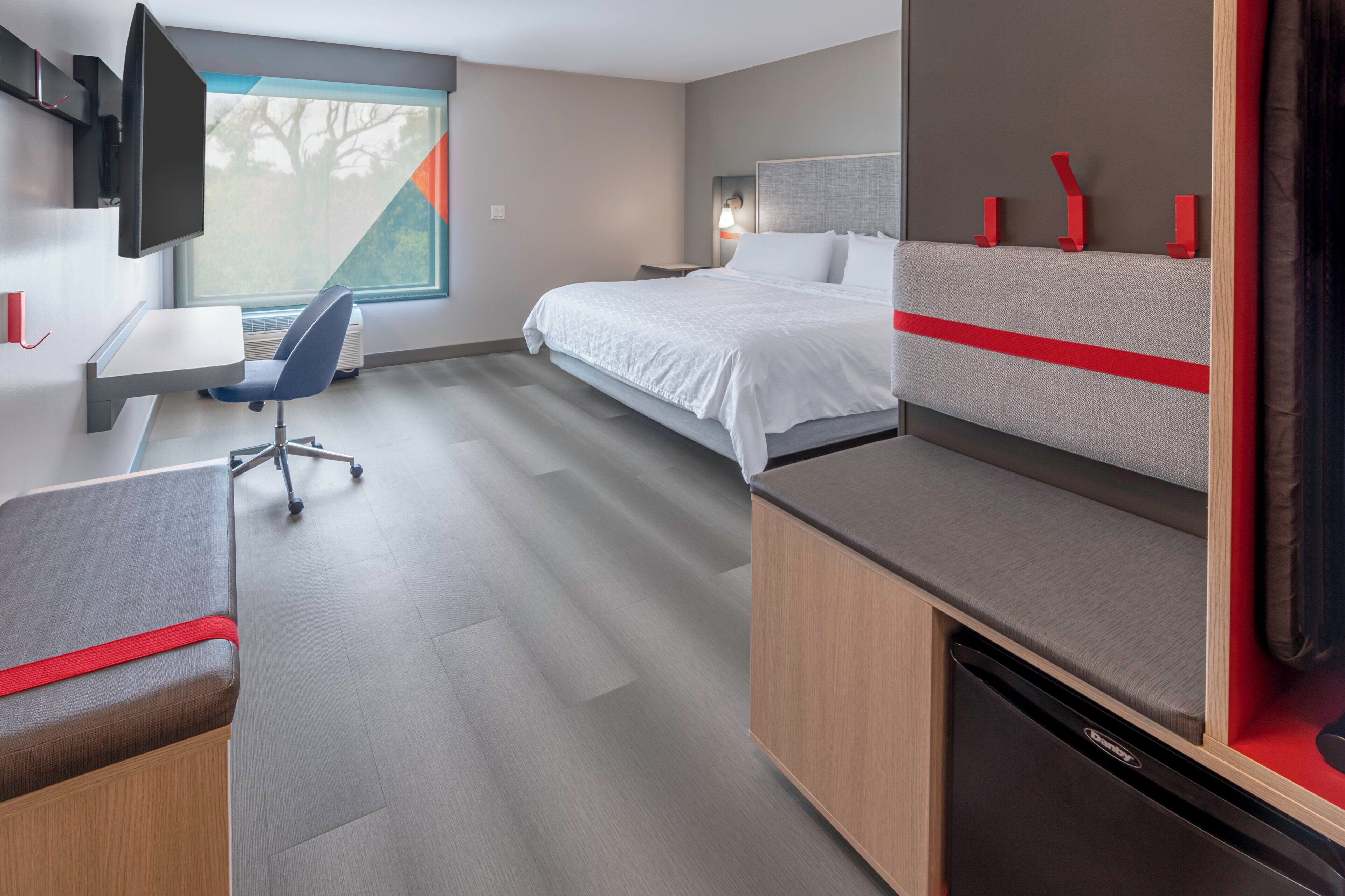 A modern hotel room with a bed, desk, chair, and a television.