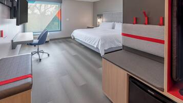 A modern hotel room with a bed, desk, chair, and a television.
