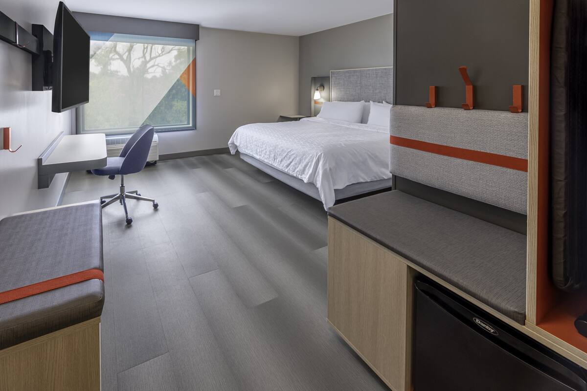 A modern hotel room with a bed, a desk, a chair, a TV, and a window.