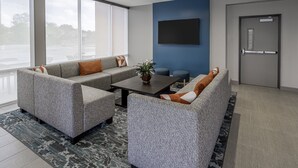 A modern lounge area with grey upholstered sofas, a central coffee table, and a flat-screen TV mounted on the wall. - avid hotel Milwaukee West Waukesha by IHG (Pewaukee)
