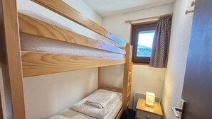 A bunk bed room with a window, a bedside table with a lamp, and a door.