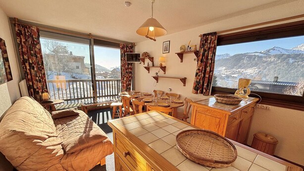 A cozy room with a bed, a dining table, and a kitchen area with a view of mountains.