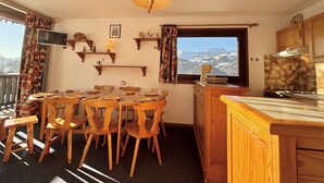 A cozy kitchen with wooden furniture, a dining area with chairs, a window with a mountain view, and a TV on the wall.