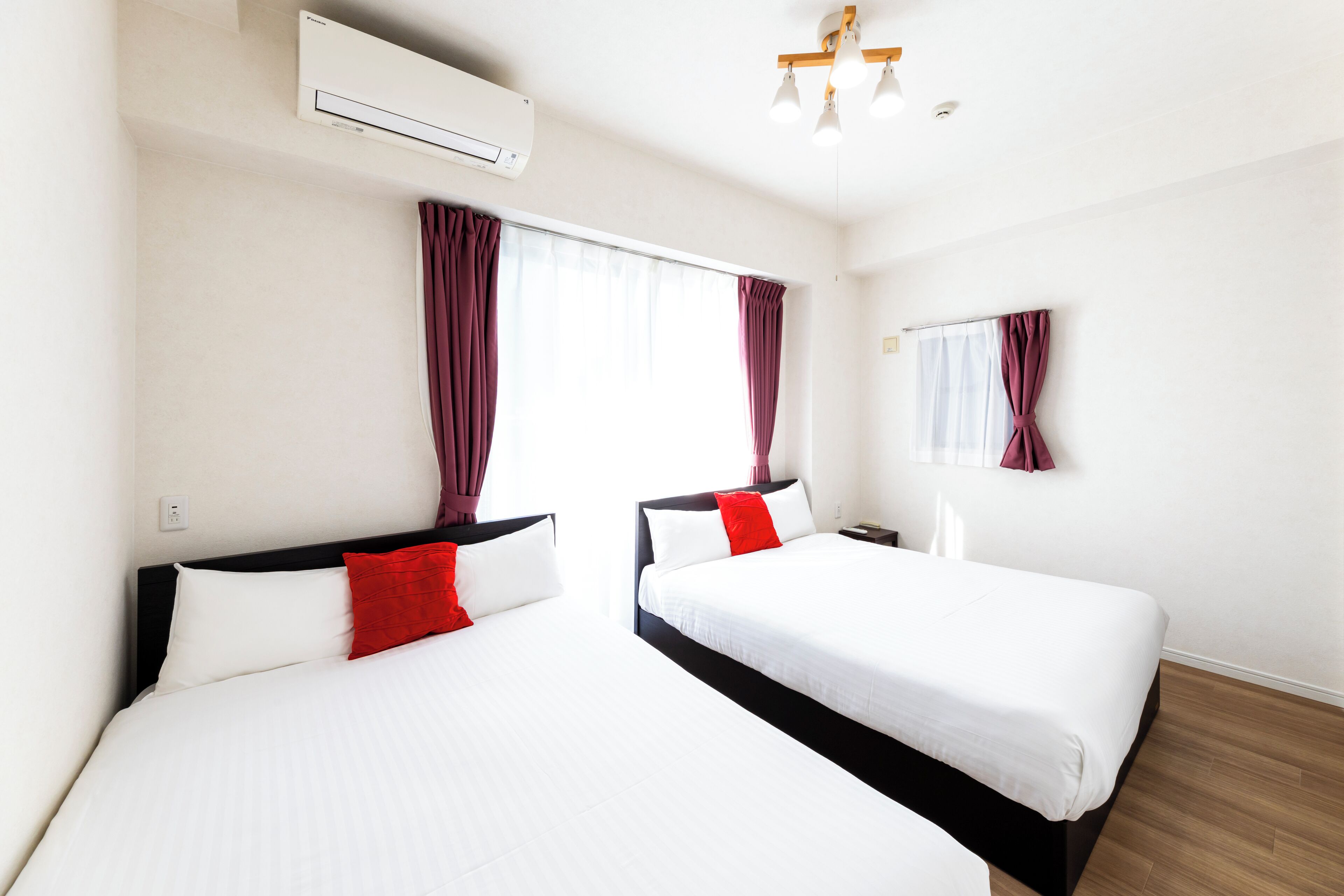 Ein Hotelzimmer mit zwei Betten, einem Deckenventilator, einer Klimaanlage und einem Fenster mit Vorhängen.