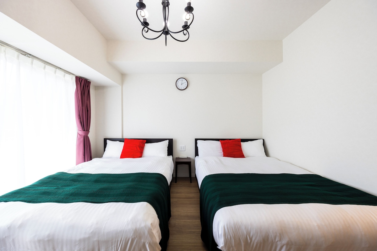 Une chambre d’hôtel avec deux lits, un lustre, une horloge et une fenêtre avec des rideaux.