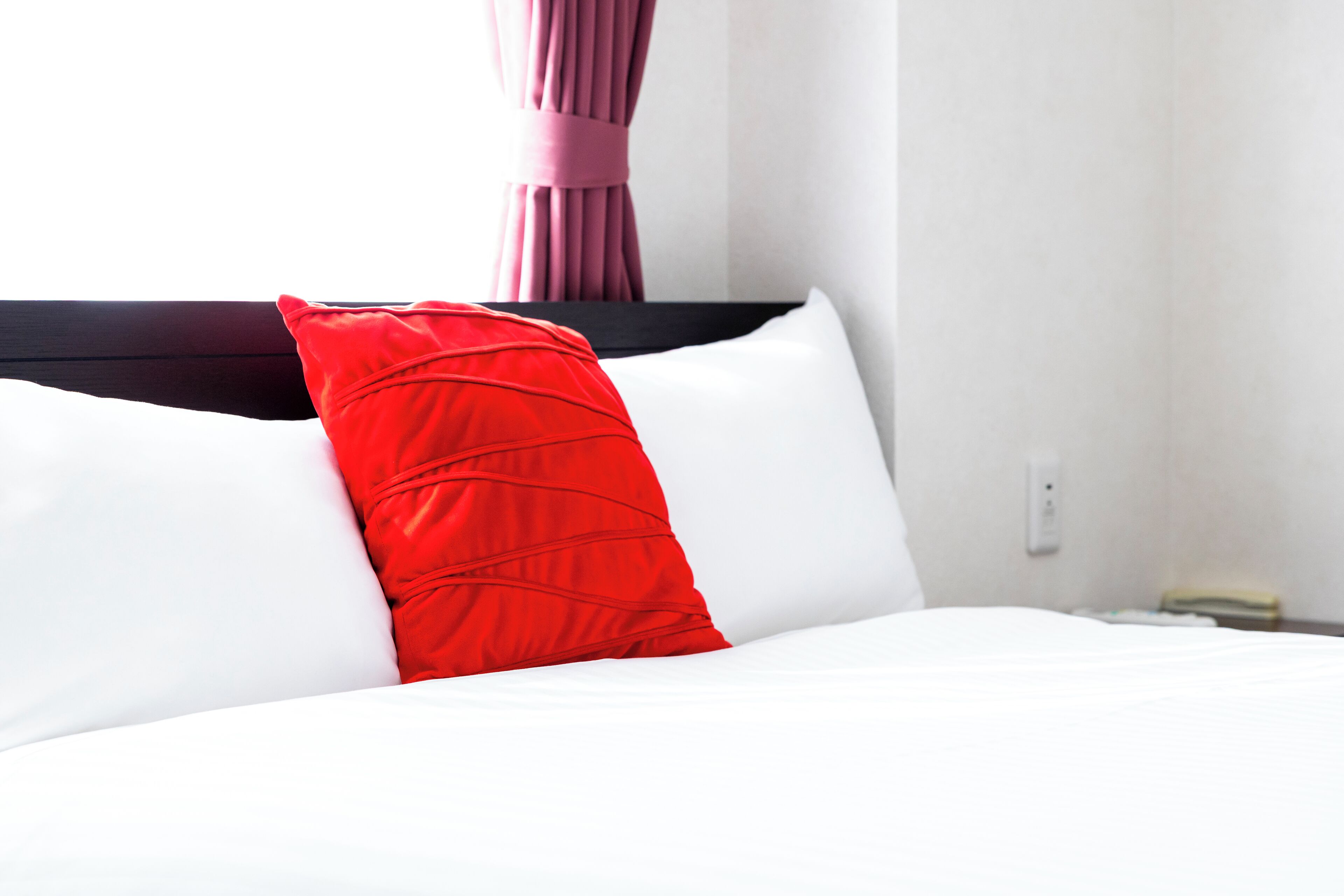 A bed with white and red pillows, a dark headboard, and a white wall with a power outlet.