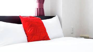 A bed with white and red pillows, a dark headboard, and a white wall with a power outlet.