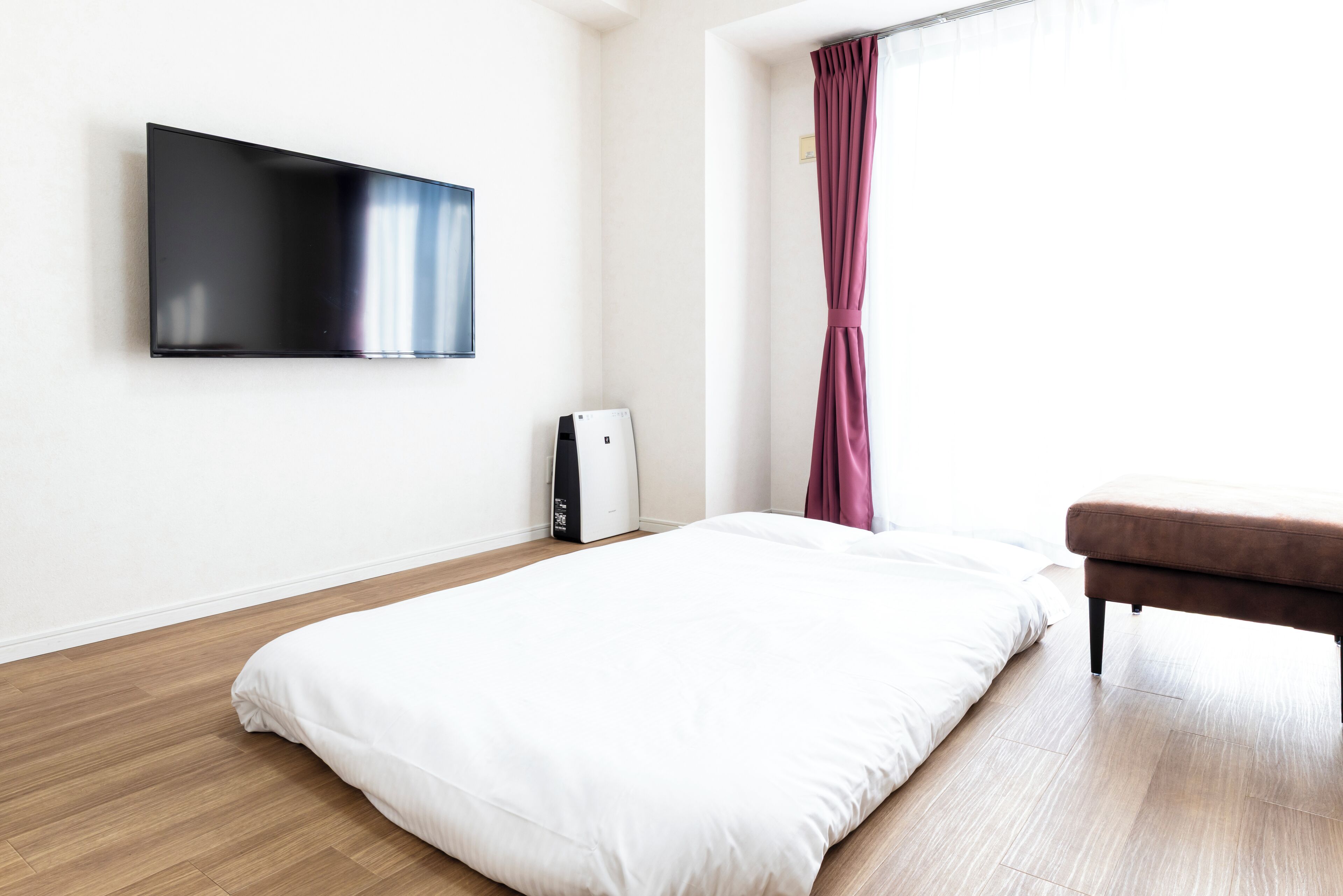 A bedroom with a bed, a TV mounted on the wall, a heater, and a window with curtains.