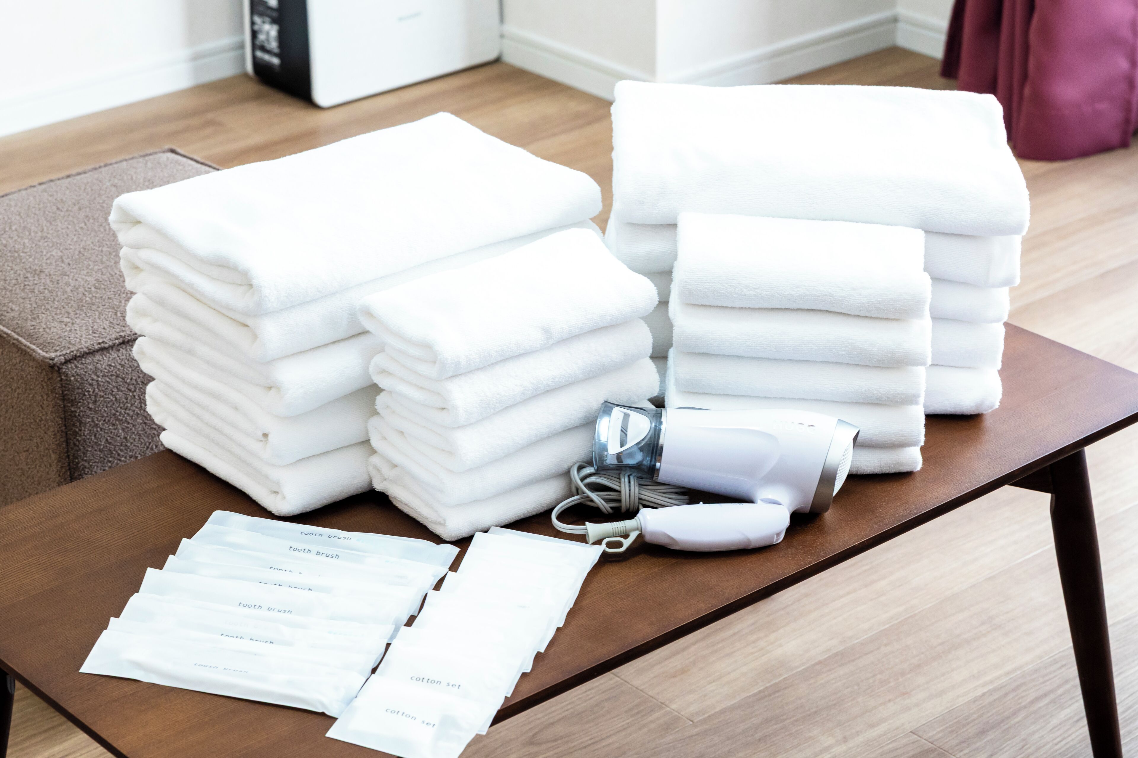 Une table bien rangée, sur laquelle on trouve des piles de serviettes blanches, un sèche-cheveux et des trousses de produits de toilette.